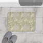Decorative bath mat with floral pattern on a tiled floor, next to slippers and a towel.