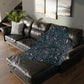Floral-patterned blanket draped over a dark brown leather sofa in a living room.