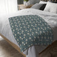 A rectangular blanket with a two-sided print featuring William Morris & Co floral patterns in shades of slate and green in a pattern called Pimpernel with a luxurious velveteen texture.