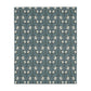 A rectangular blanket with a two-sided print featuring William Morris & Co floral patterns in shades of slate and green in a pattern called Pimpernel with a luxurious velveteen texture.