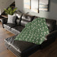 A rectangular blanket with a two-sided print featuring William Morris & Co floral patterns in shades of slate and green in a pattern called Pimpernel with a luxurious velveteen texture.