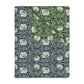 A rectangular blanket with a two-sided print featuring William Morris & Co floral patterns in shades of slate and green in a pattern called Pimpernel with a luxurious velveteen texture.