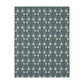 A rectangular blanket with a two-sided print featuring William Morris & Co floral patterns in shades of slate and green in a pattern called Pimpernel with a luxurious velveteen texture.