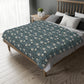 A rectangular blanket with a two-sided print featuring William Morris & Co floral patterns in shades of slate and green in a pattern called Pimpernel with a luxurious velveteen texture.