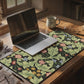 A large desk mat with a green William Morris & Co floral pattern, displayed on a desk with a keyboard and mouse, with a monitor above it.