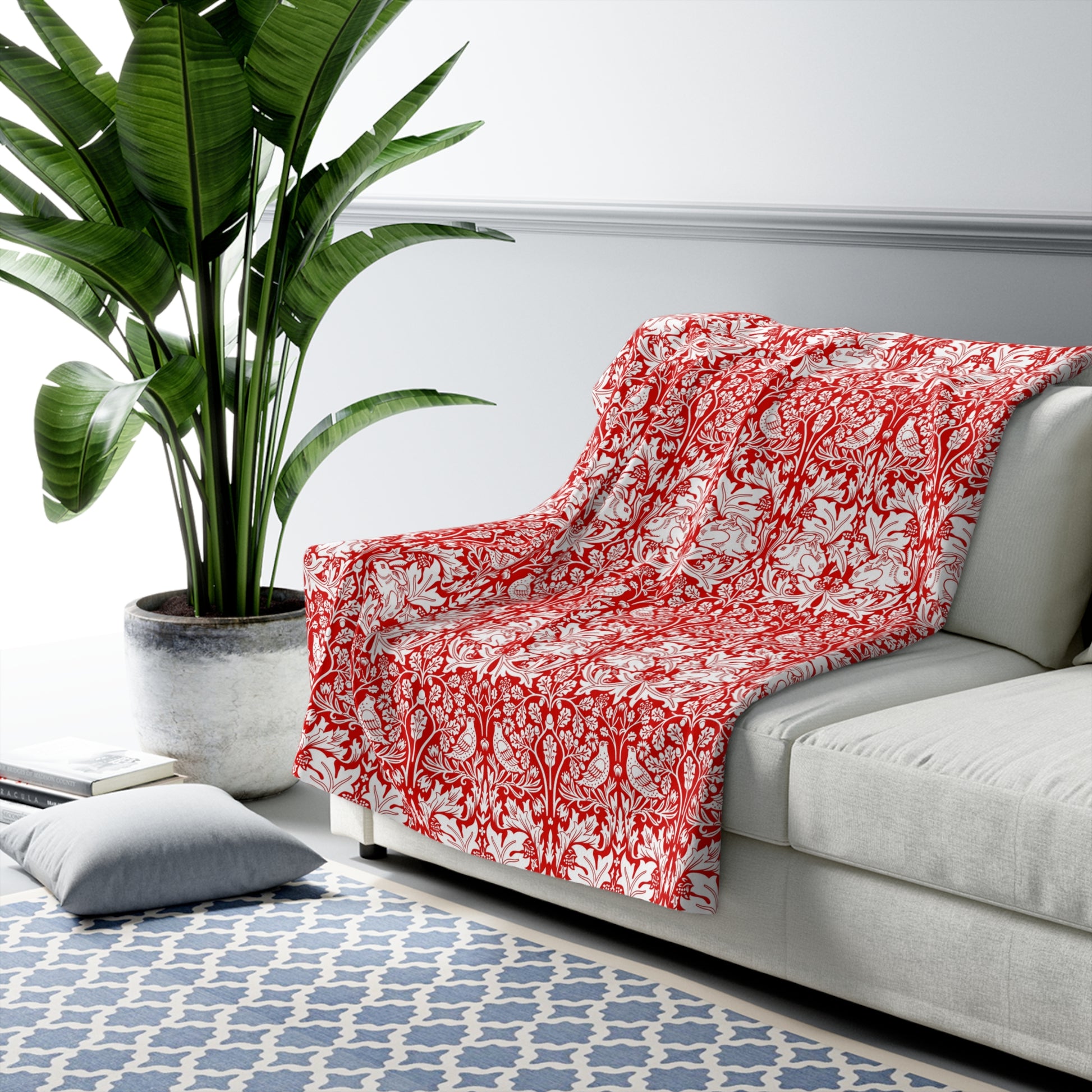 Red floral blanket on a gray sofa with a plant and rug in the background