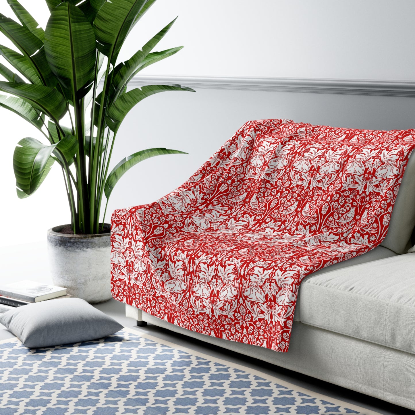Red floral-patterned blanket draped over a gray sofa in a living room with a plant and rug.