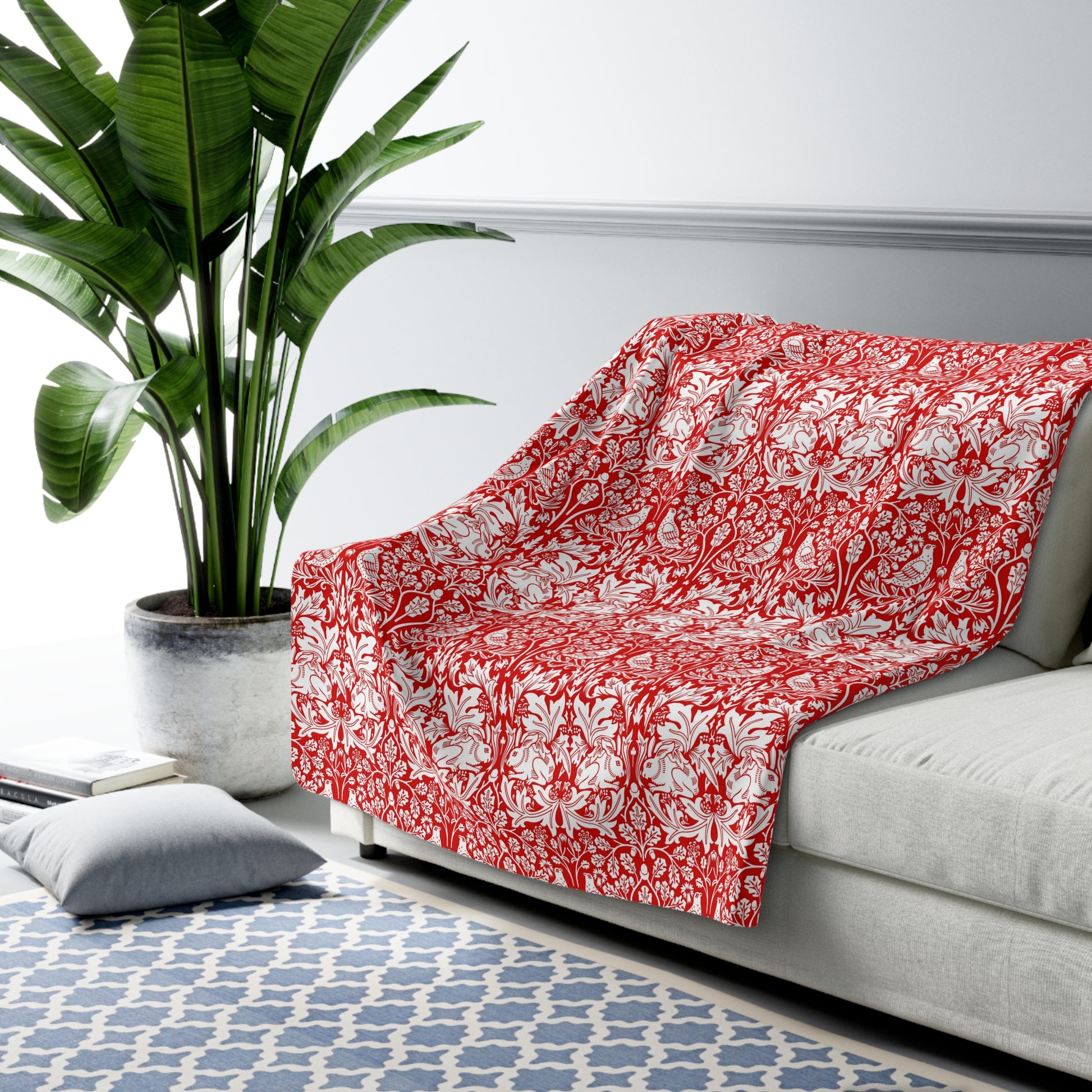 Red floral-patterned blanket draped over a gray sofa in a living room with a plant and rug.