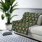 A plush fleece blanket with a yellow chrysanthemum pattern on a green background, laid flat.