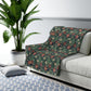 Floral-patterned throw blanket draped over a white sofa in a living room with a plant and rug.