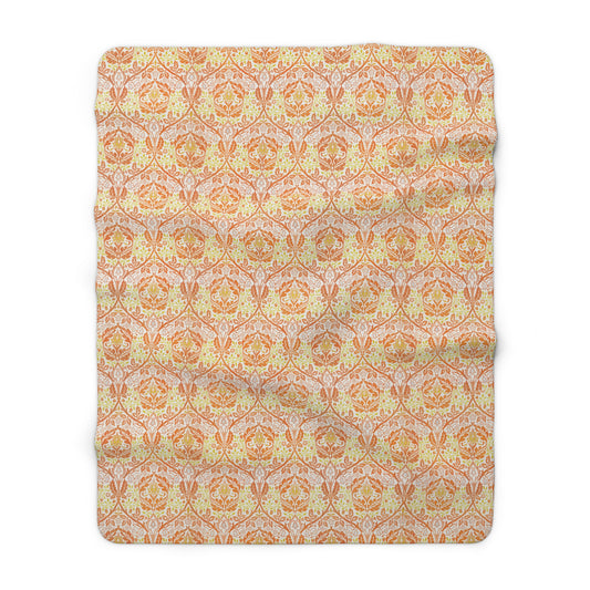 A plush fleece blanket with a geometric pattern in orange and cream colours, laid out flat.