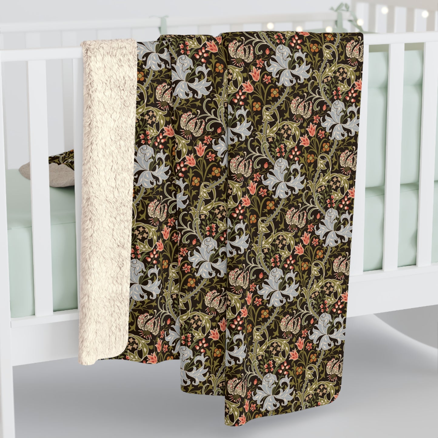 A baby blanket draped over a white crib, showing a dark brown and olive green floral and botanical pattern with white flowers and coral accents, and a soft cream sherpa backing.