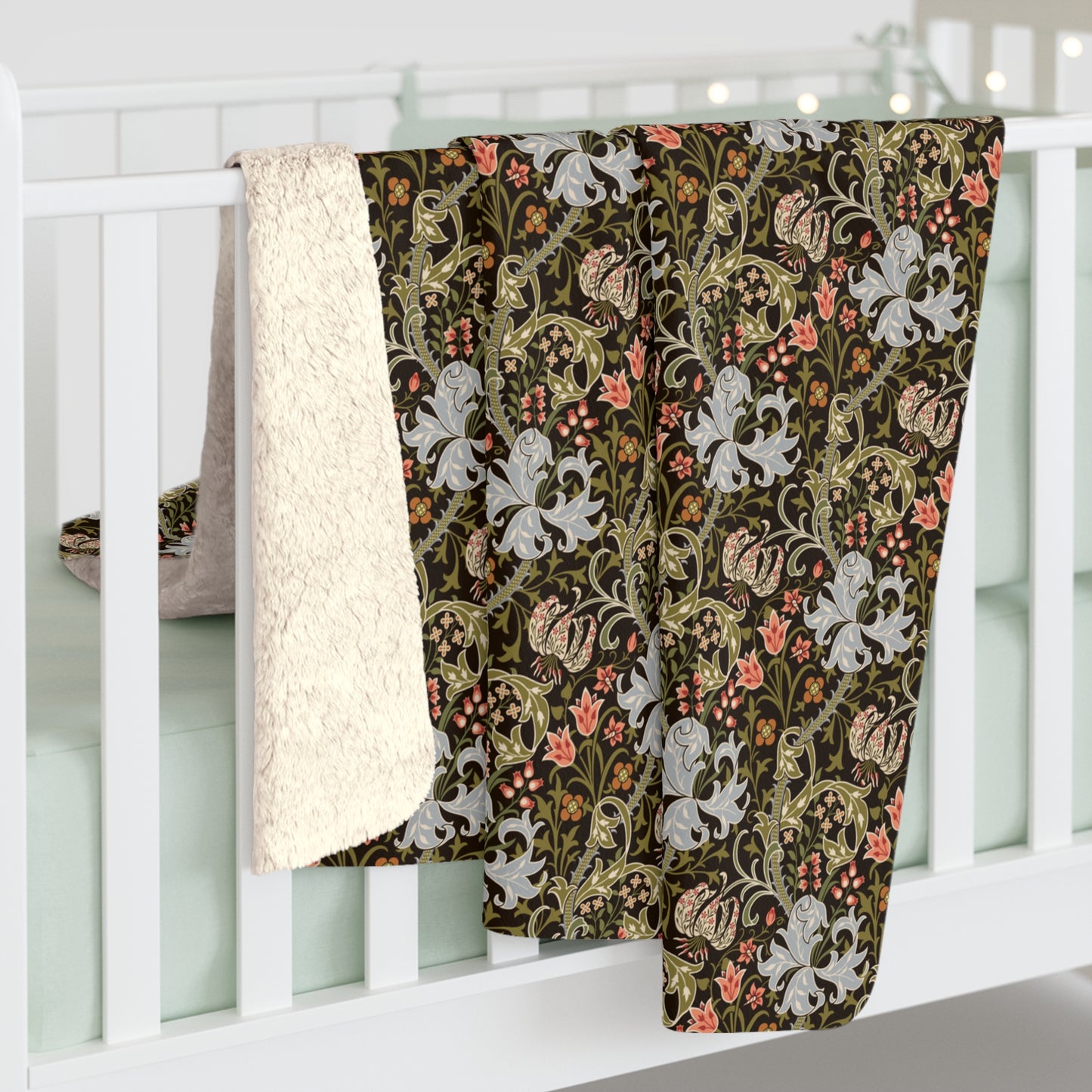 A folded baby blanket draped over a white crib, showing a dark brown and olive green floral pattern with white lilies and pink accents, alongside a soft cream sherpa fleece backing.