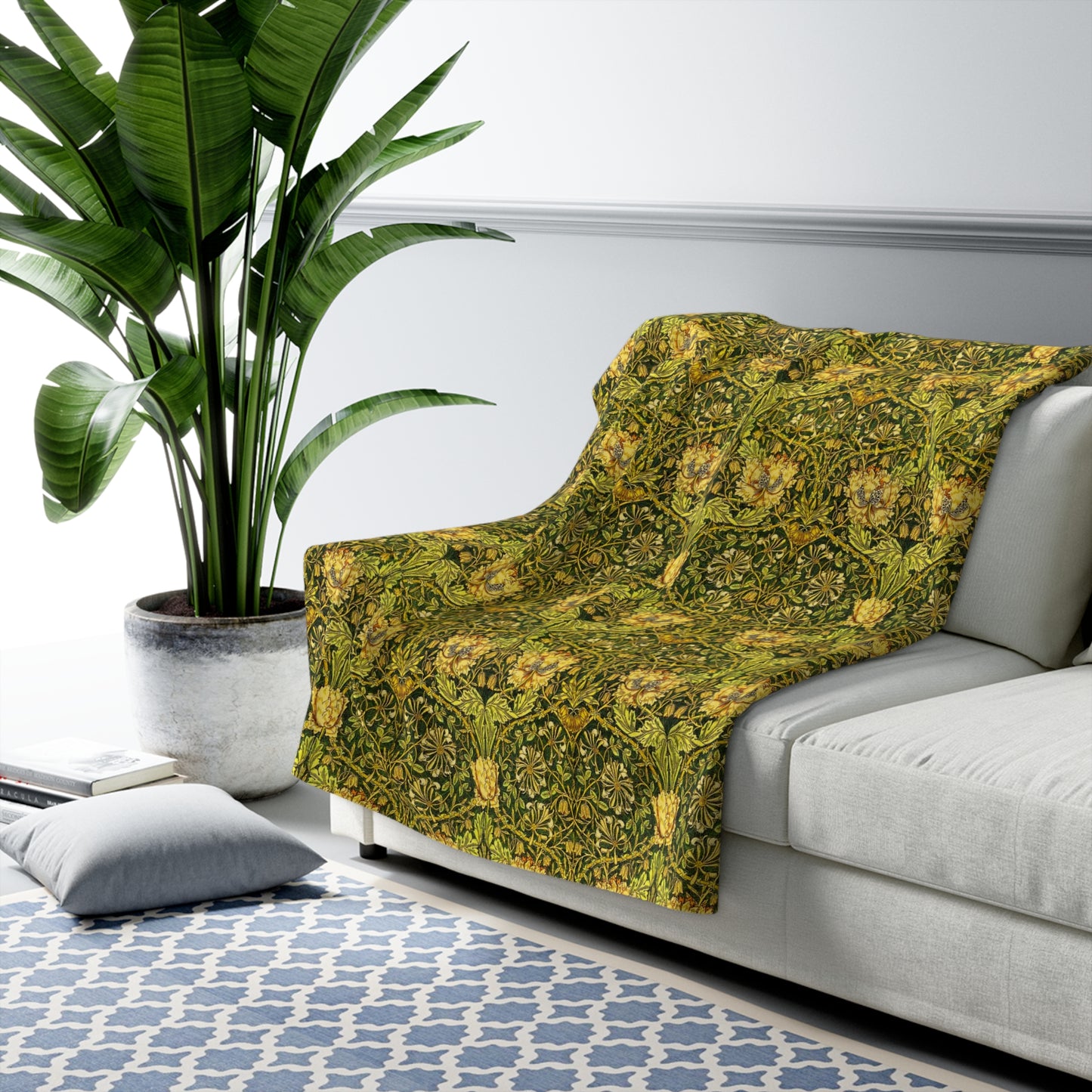Green patterned throw blanket on a gray sofa with a plant and rug in the background