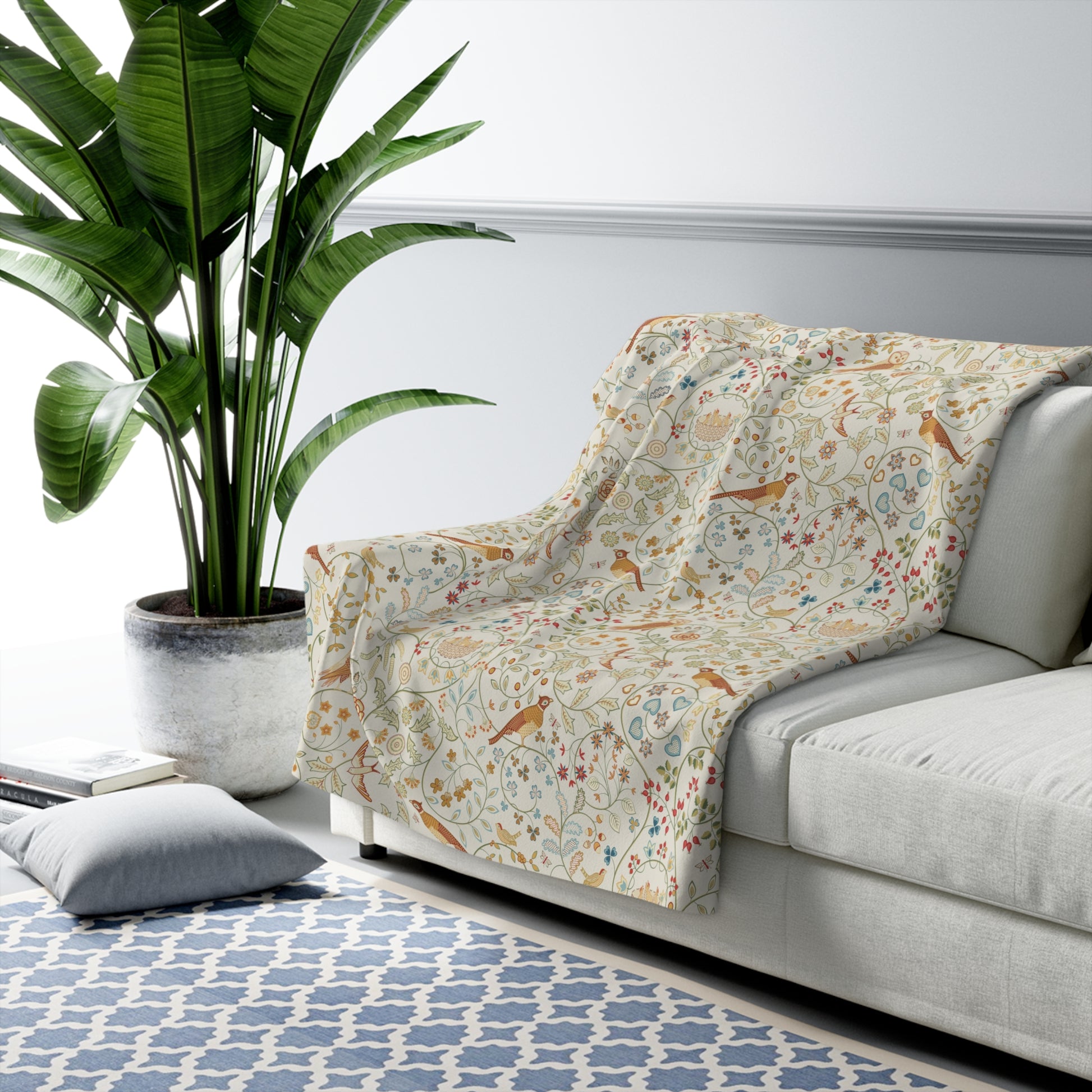 Floral-patterned throw blanket draped over a sofa in a living room with a plant and rug.