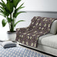 A plush fleece blanket with a floral pattern in a purple hue, inspired by William Morris, displayed on a white background.