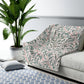 Gray patterned throw blanket draped over a sofa in a living room with a plant and rug.