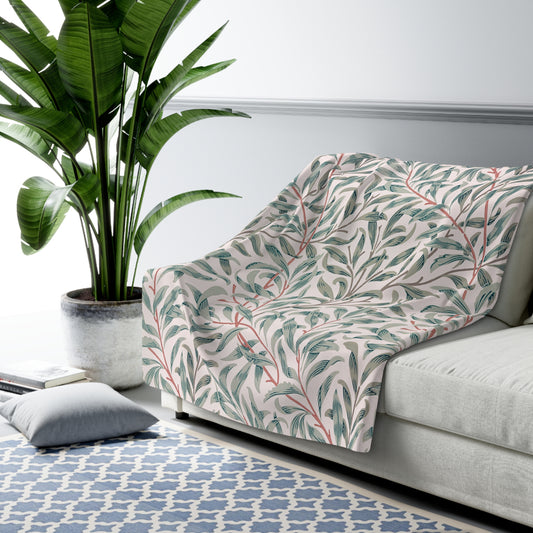 Gray patterned throw blanket draped over a sofa in a living room with a plant and rug.