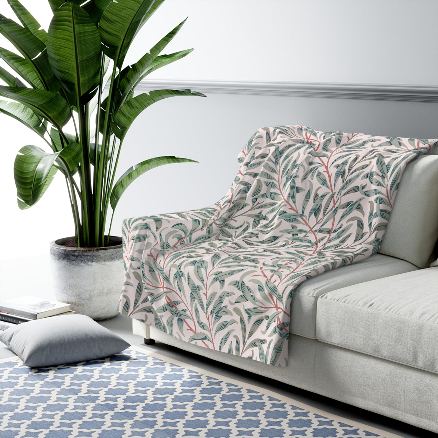 Floral-patterned blanket draped over a gray sofa in a living room with a plant and rug.