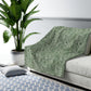 A green Sherpa fleece blanket with a floral pattern inspired by William Morris, displayed flat.