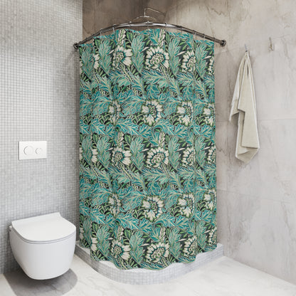 A bathroom scene showing a shower curtain with a teal, green, and white botanical leaf pattern hanging in a shower. The bathroom also features a white vanity with a marble countertop, a mirror, and a blue-gray accent wall.