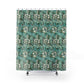 A bathroom scene showing a shower curtain with a teal, green, and white botanical leaf pattern hanging in a shower. The bathroom also features a white vanity with a marble countertop, a mirror, and a blue-gray accent wall.