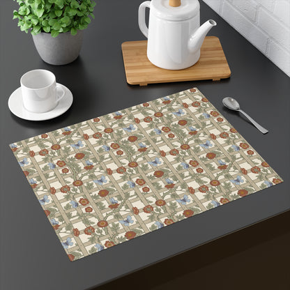 A rectangular placemat with a vintage floral pattern in muted brown, blue, and green tones on a cream background, styled on a dark tabletop next to a white teapot, teacup, and spoon.