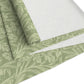 A green table runner with a floral William Morris & Co pattern, featuring acorns and oak leaves, laid out on a wooden dining table with cutlery and a vase of pink flowers in the background. 