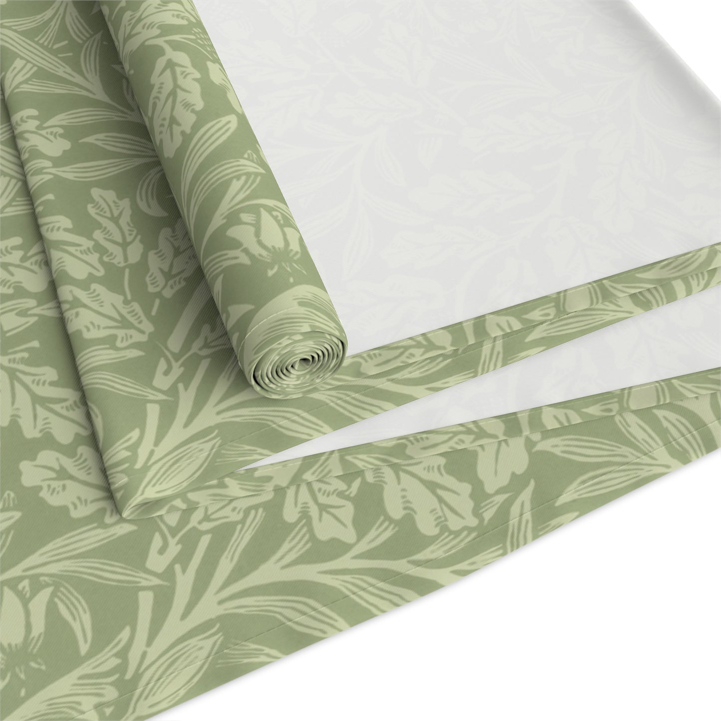 A green table runner with a floral William Morris & Co pattern, featuring acorns and oak leaves, laid out on a wooden dining table with cutlery and a vase of pink flowers in the background. 