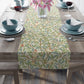 A table runner with a Victorian William Morris & Co floral design in green, blue, and brown colours, laid out on a dining table.