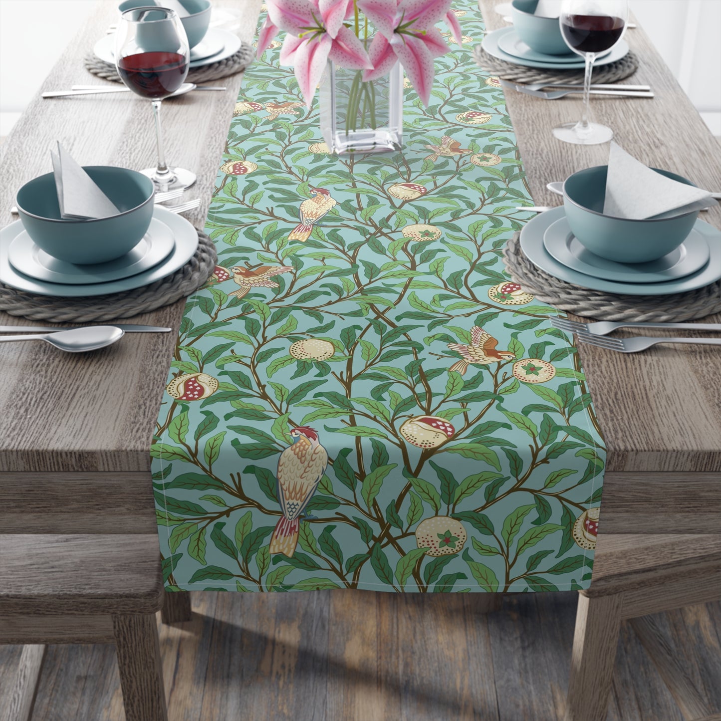 A tiffany blue table runner with a William Morris & Co floral and bird design laid out on a dining table with dishes and cutlery.