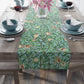 A tiffany blue table runner with a floral and bird design laid out on a dining table with dishes and cutlery.