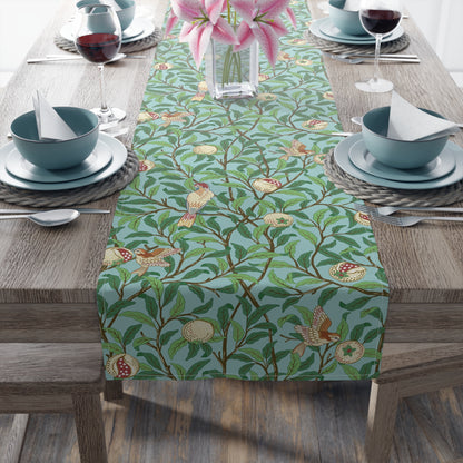 A tiffany blue table runner with a floral and bird design laid out on a dining table with dishes and cutlery.