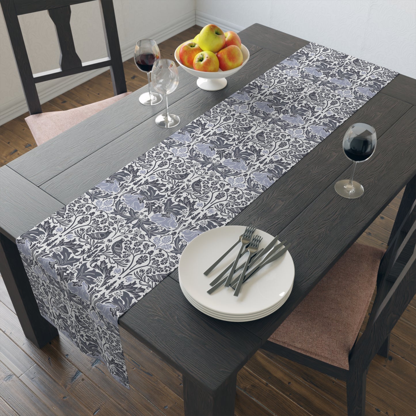 Dining table with a floral-patterned gray table runner, plates, forks, and glasses.