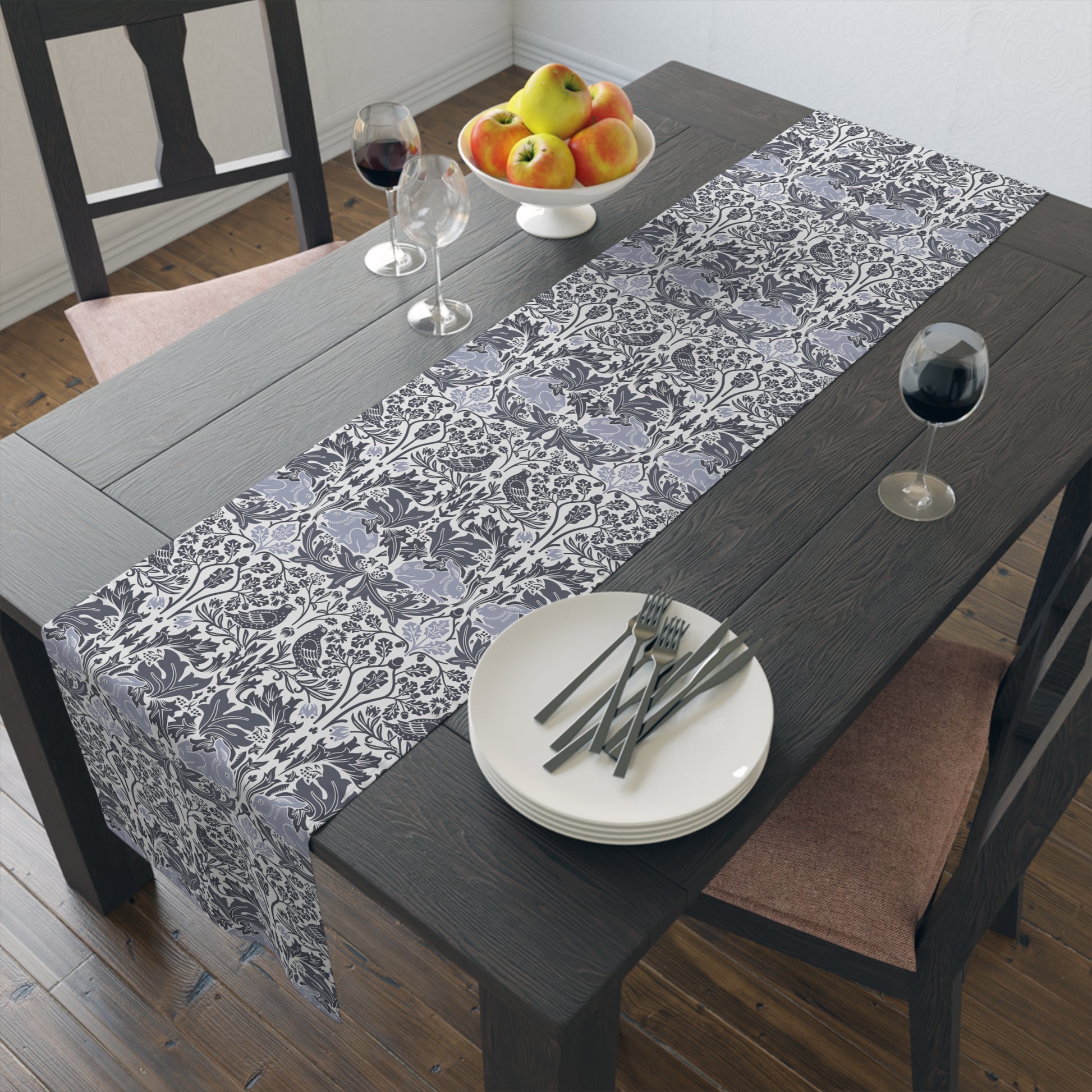 Dining table with a floral-patterned gray table runner, plates, forks, and glasses.