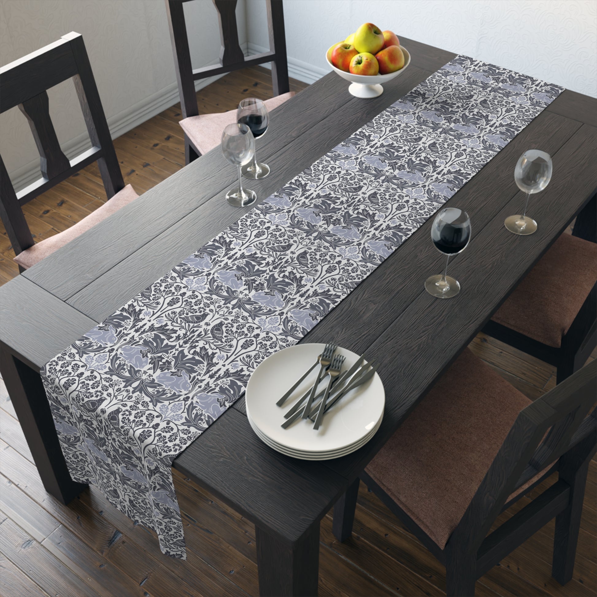 Dining table set with a floral runner, plates, and glasses in a room.