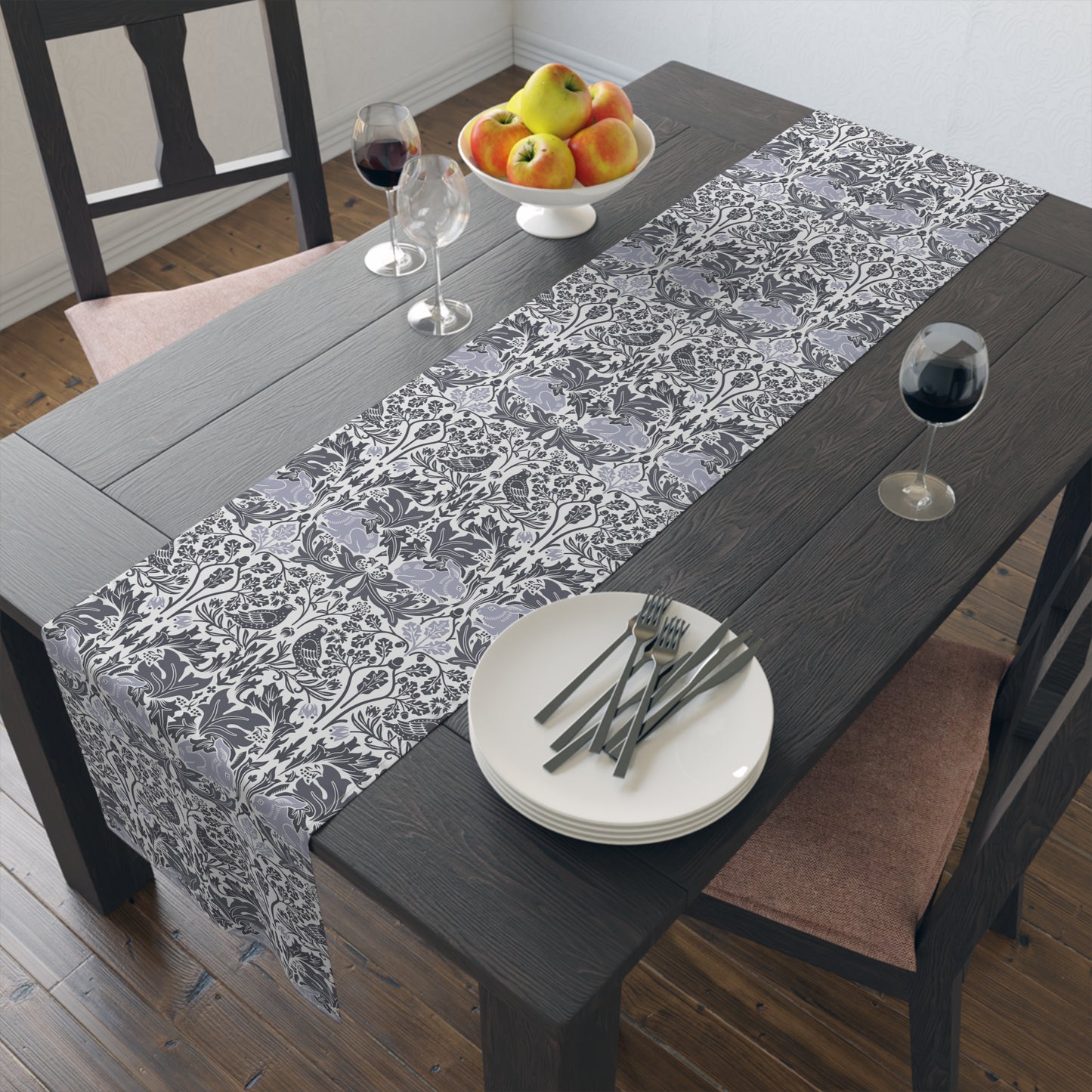Dining table with a floral patterned table runner, plates, forks, and glasses.