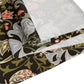 A table runner with a floral William Morris & Co pattern in shades of green, gold, and other colours, laid out on a dining table with dishes and glasses arranged on top.