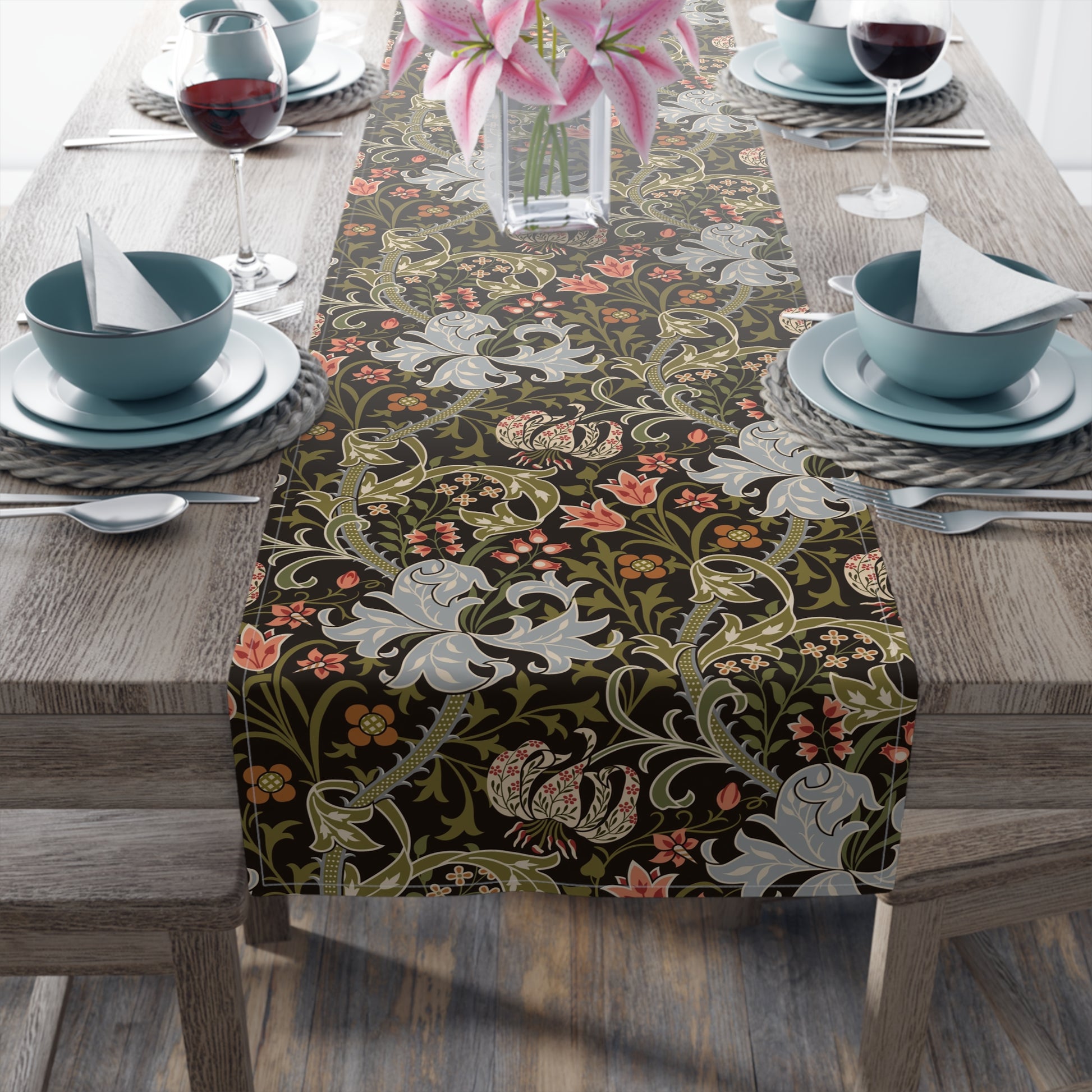 A table runner with a floral pattern in shades of green, gold, and other colors, laid out on a dining table with dishes and glasses arranged on top.
