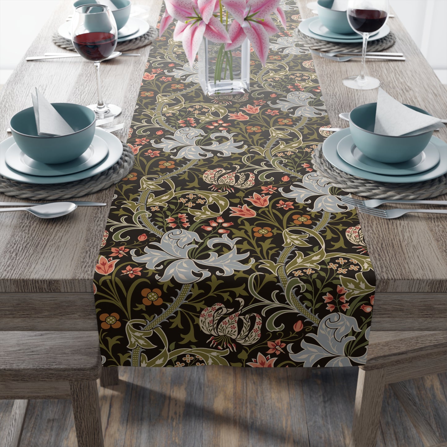 A table runner with a floral pattern in shades of green, gold, and other colors, laid out on a dining table with dishes and glasses arranged on top.