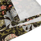 A table runner with a floral William Morris & Co pattern in shades of green, gold, and other colours, laid out on a dining table with dishes and glasses arranged on top.