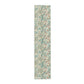 A table runner with a floral William Morris & Co pattern in green, beige, and gold colours, laid out on a dining table.