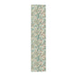 A table runner with a floral William Morris & Co pattern in green, beige, and gold colours, laid out on a dining table.