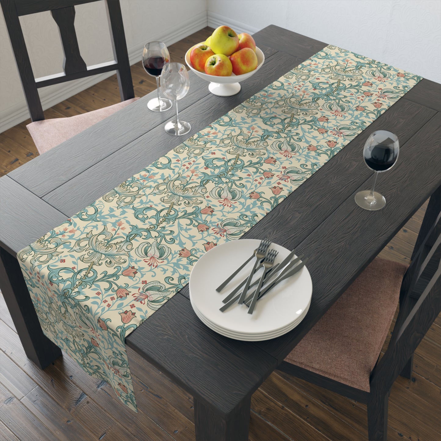 A table runner with a floral William Morris & Co pattern in green, beige, and gold colours, laid out on a dining table.