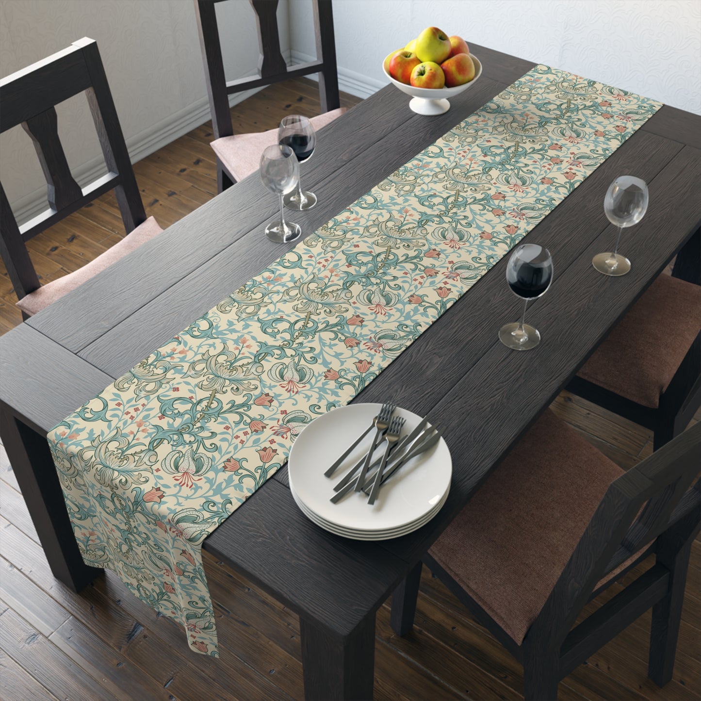 A table runner with a floral William Morris & Co pattern in green, beige, and gold colours, laid out on a dining table.