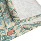 A table runner with a floral William Morris & Co pattern in green, beige, and gold colours, laid out on a dining table.