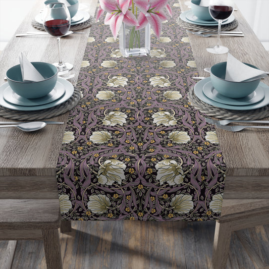 A table runner with a floral William Morris & Co pattern in purple, gold, and green colours, laid out on a dining table.