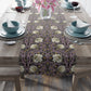 A table runner with a floral pattern in purple, gold, and green colors, laid out on a dining table.