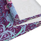 A multicolored table runner with a floral William Morris & Co pattern in pink and green on a blue background, displayed on a table with dishes and cutlery.
