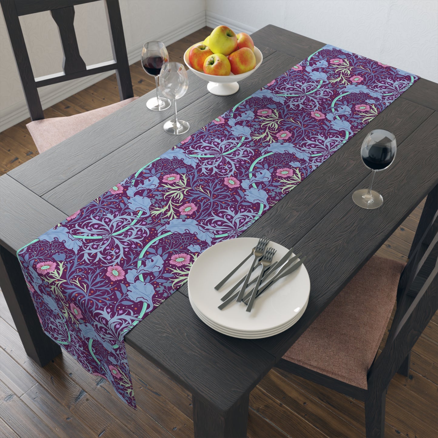 A multicolored table runner with a floral William Morris & Co pattern in pink and green on a blue background, displayed on a table with dishes and cutlery.